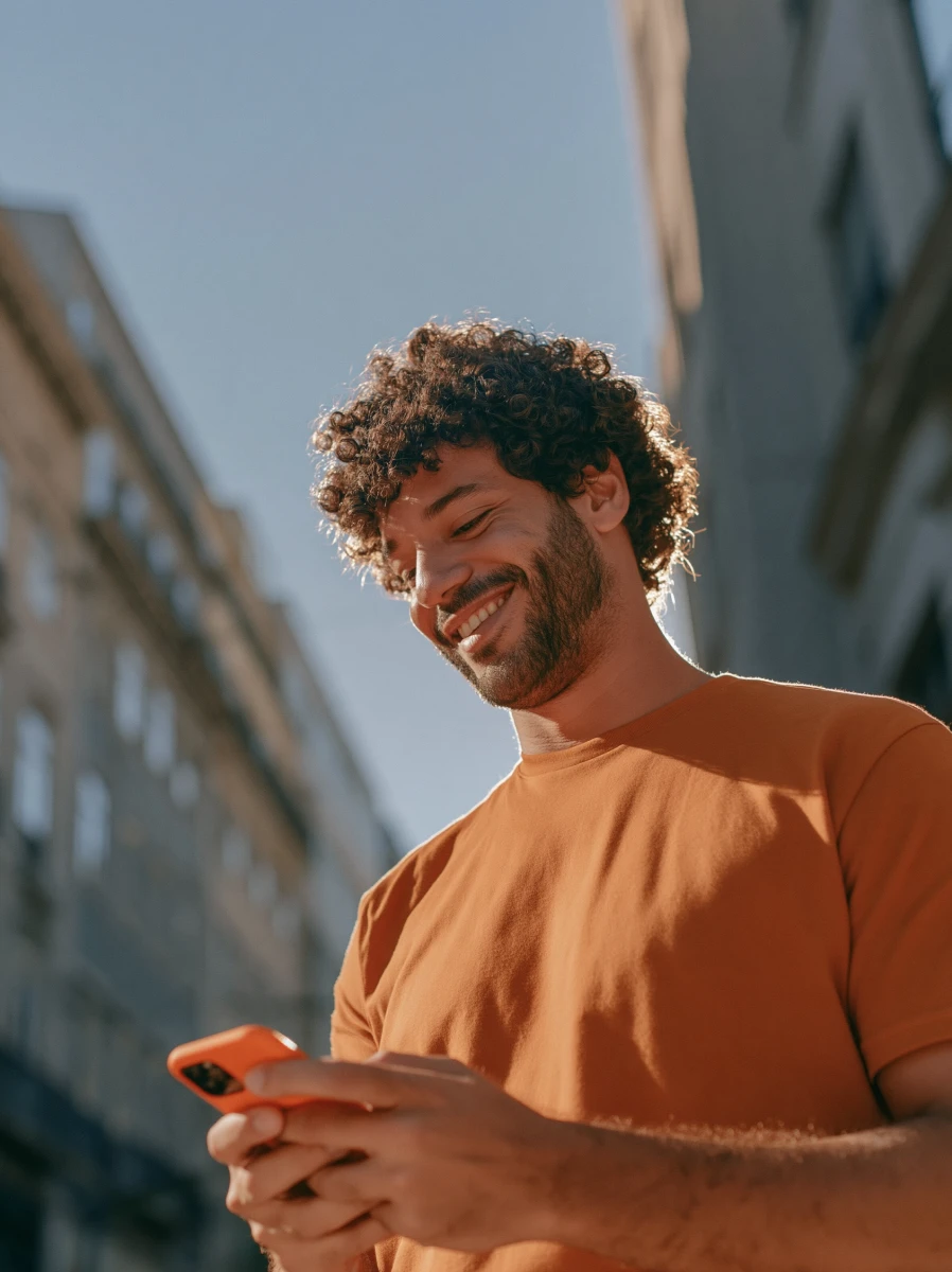 Homem sorrindo enquanto usa o celular na rua